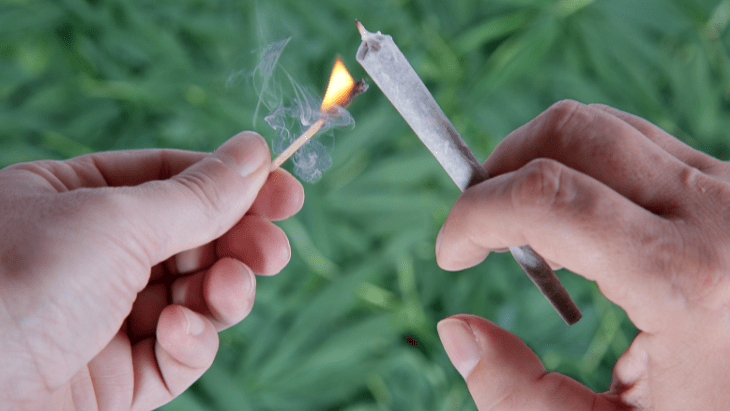 hands holding a cannabis joint and a lit match